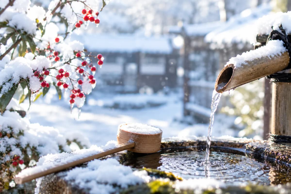 雪の積もった竹の筧から手水鉢に注ぐ水