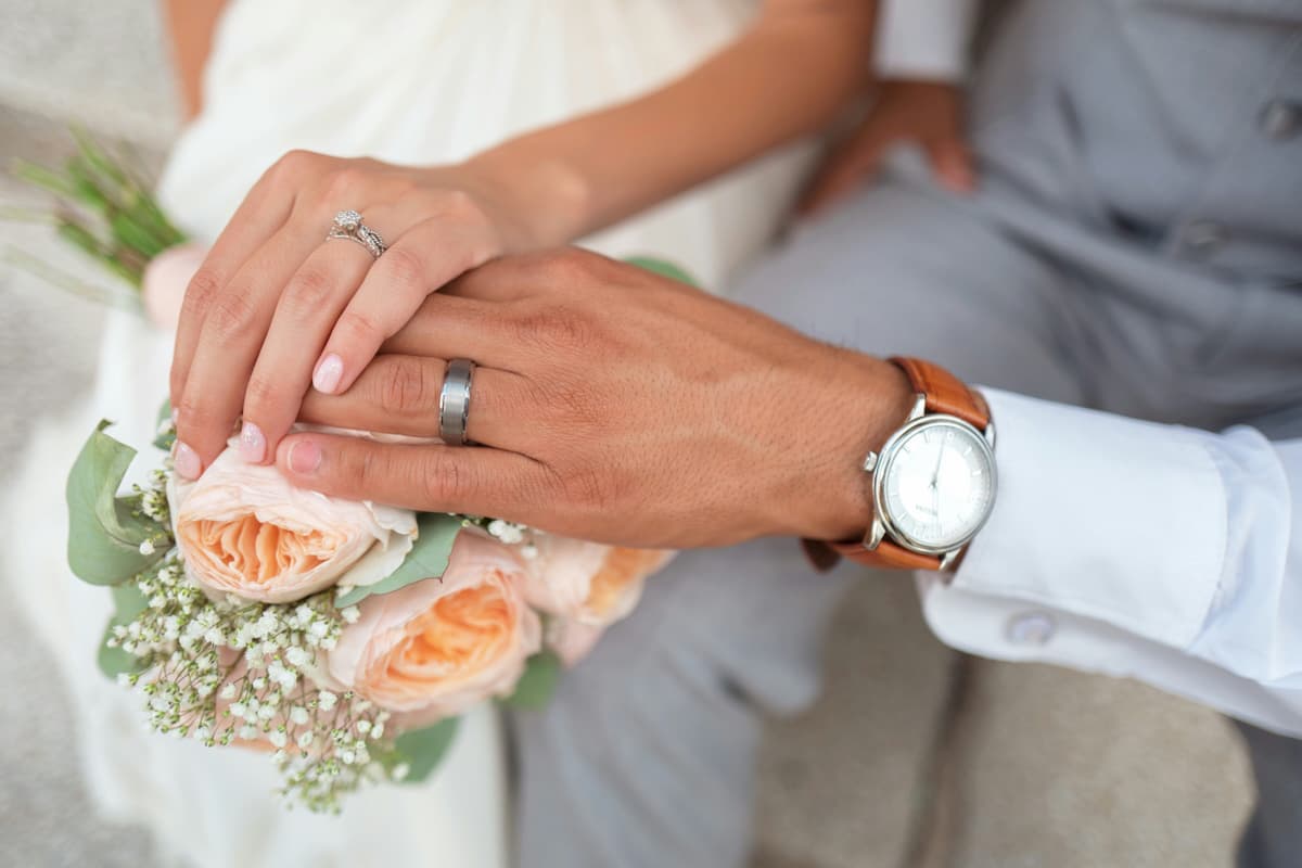 結婚指輪をはめた夫婦の手とブーケ