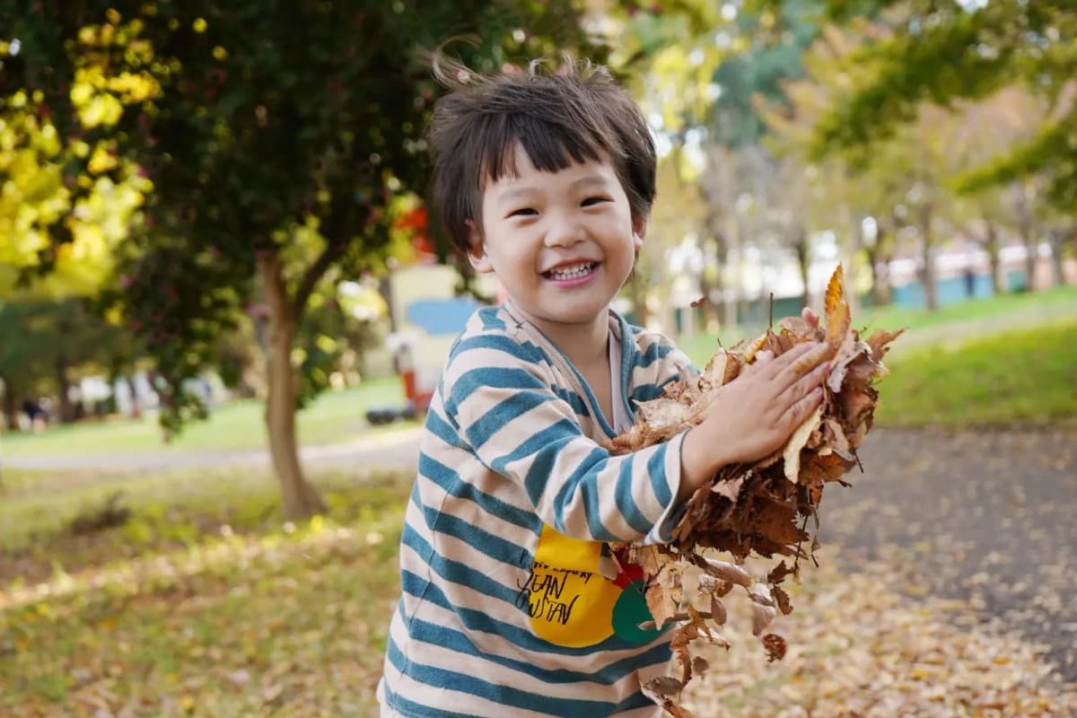 公園で落ち葉を持って笑う男の子