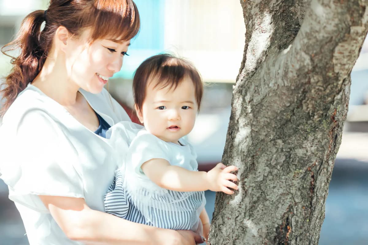 木のそばで子どもを抱っこする母親