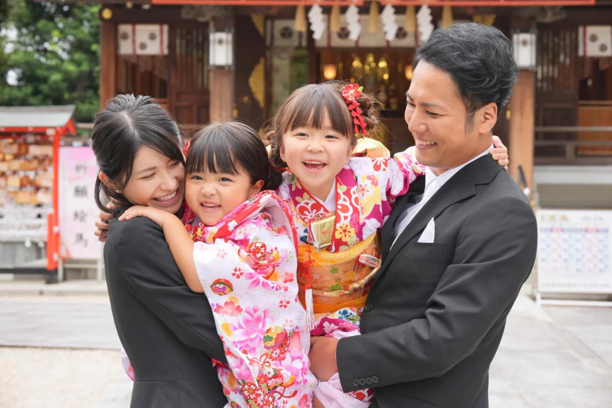 神社で着物の姉妹を抱きしめる両親