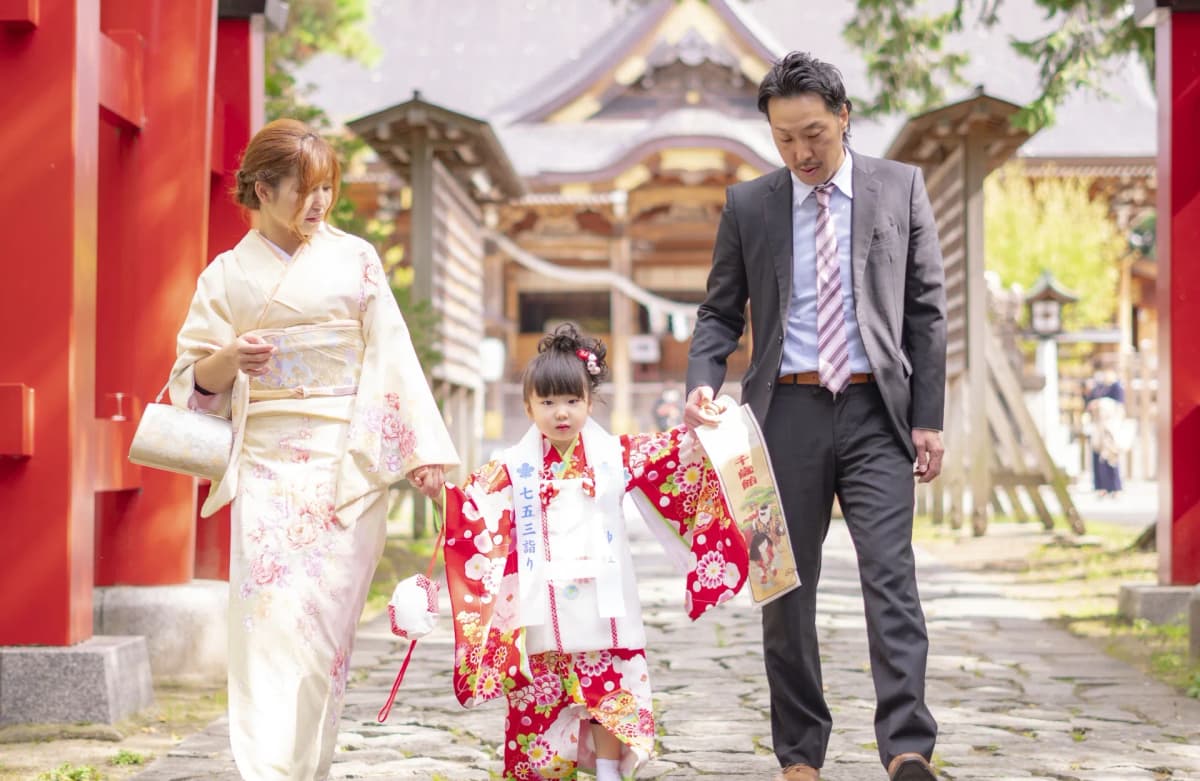 神社の参道を晴れ着の子どもと手をつないで歩く両親
