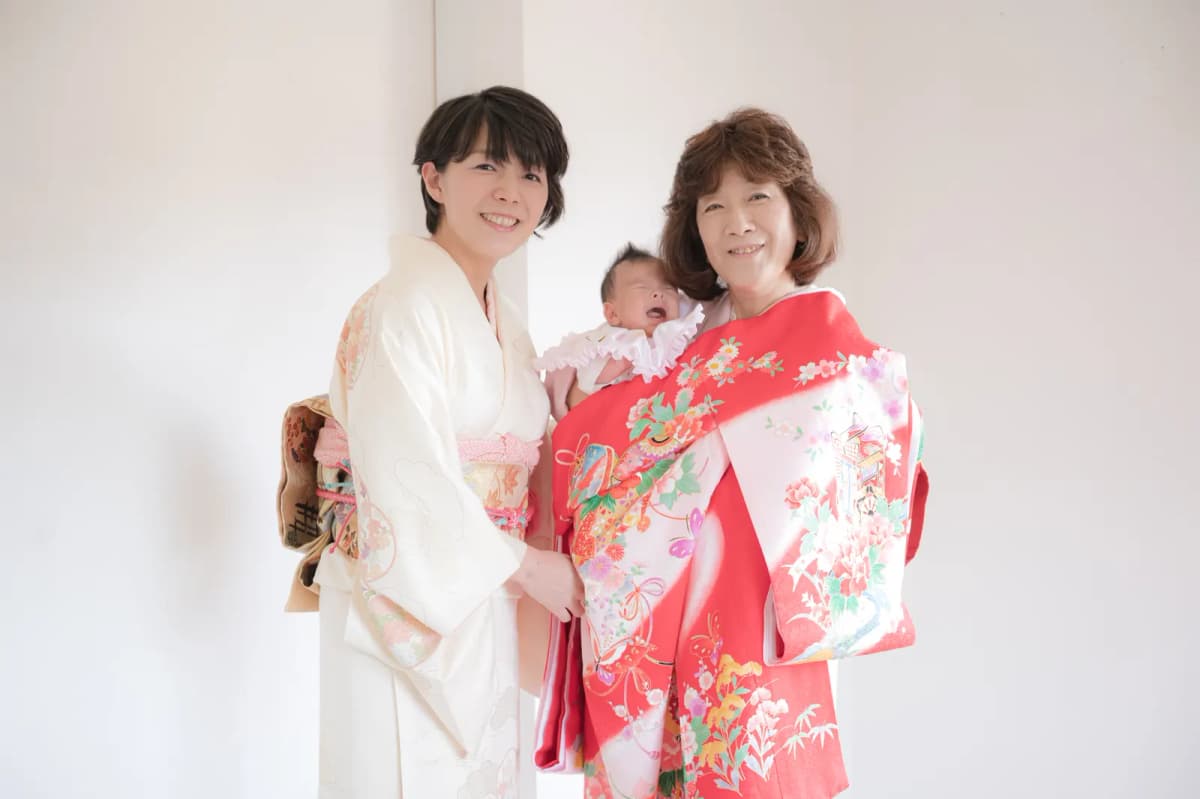 祝い着を掛けた赤ちゃんを抱く祖母と、着物姿の母親