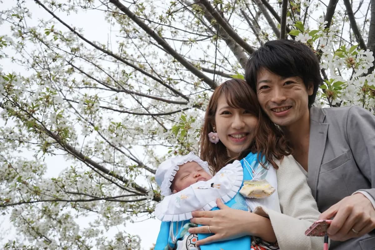 満開の桜の下で赤ちゃんを囲む夫婦