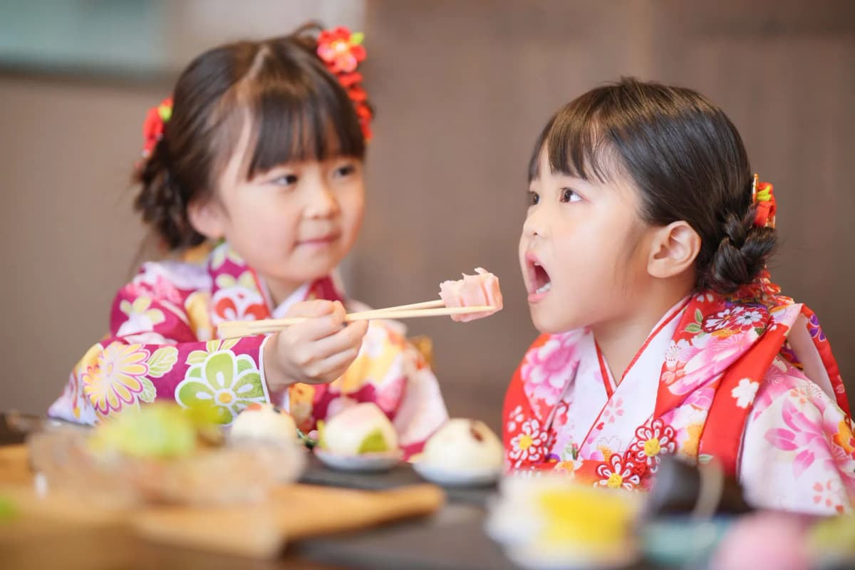 お祝いの料理を食べる着物の姉妹